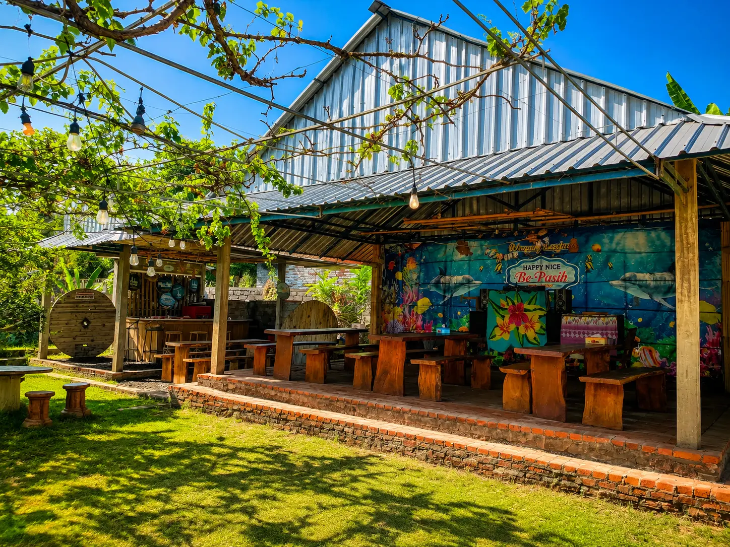 Happy Nice Be Pasih food stall with wooden tables and tropical murals